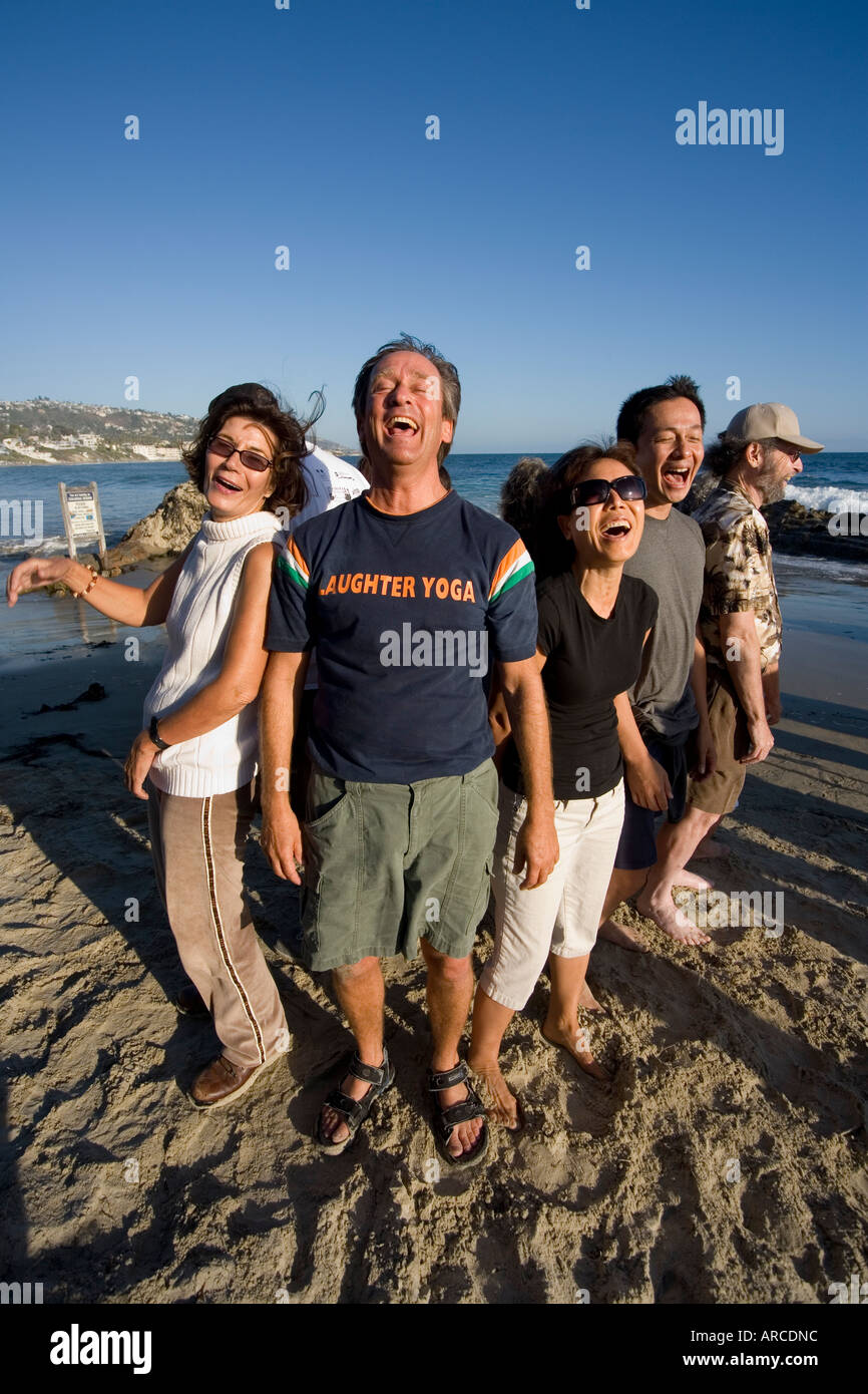 Il leader di una risata Yoga Club imposta un esempio per i suoi membri come si incontrano in riva al mare Foto Stock