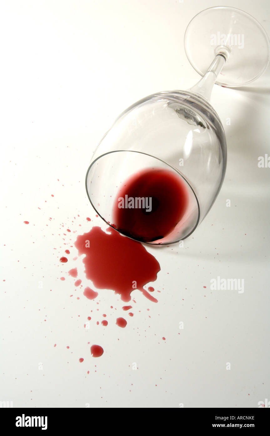 Vetro e schizzi di vino rosso su una superficie bianca Foto Stock