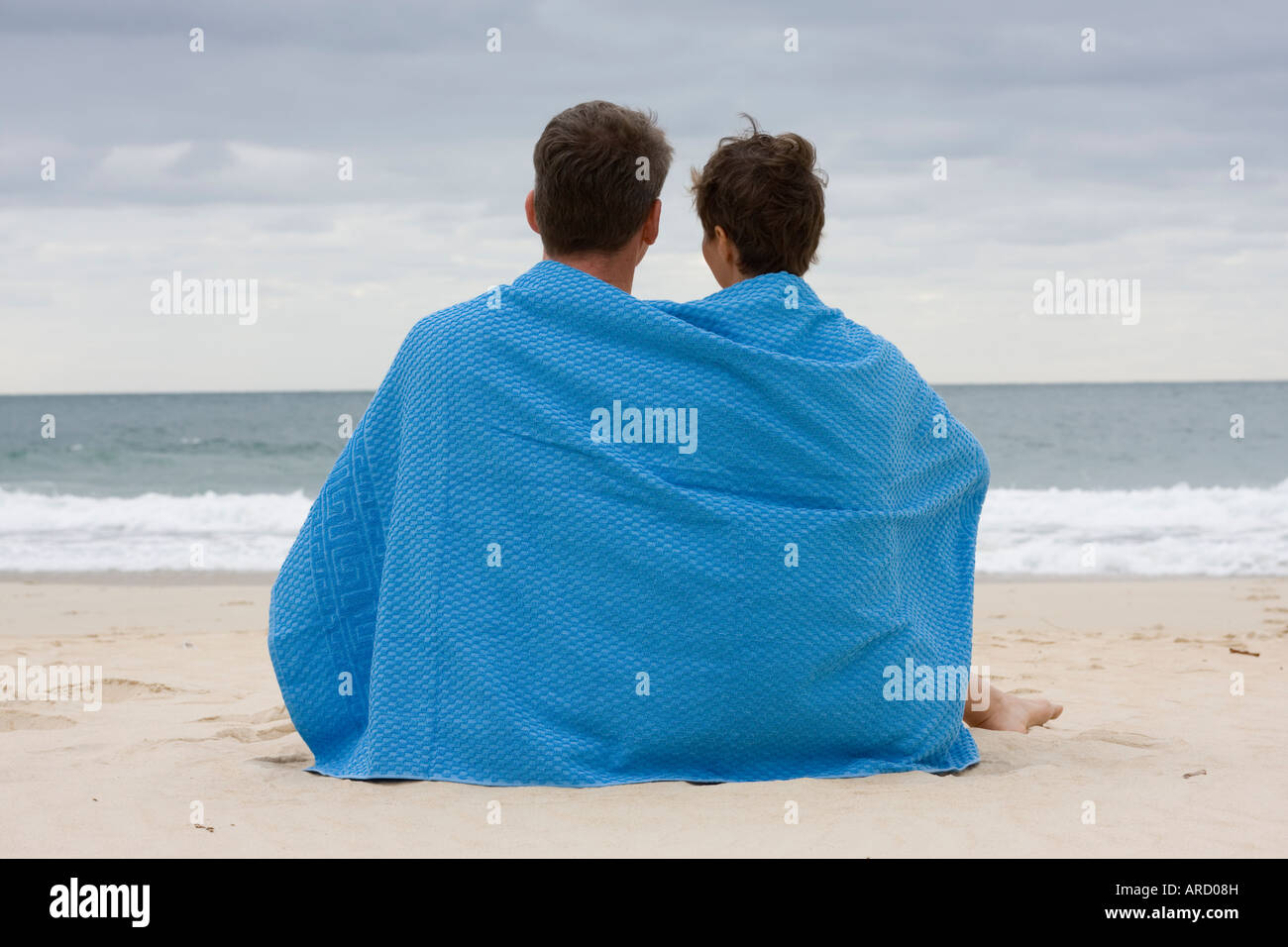 Giovane seduto sulla spiaggia con un asciugamano blu Foto Stock