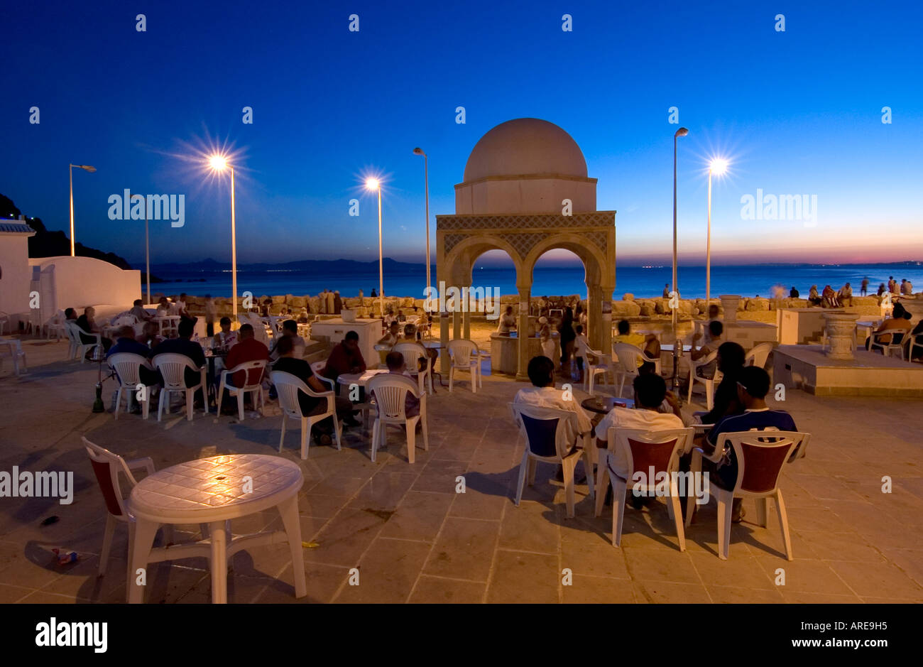 Scena di strada al tramonto nel piccolo villaggio mediterraneo di Korbous: gente seduta in un bar per fumatori waterpipe; in Tunisia. Foto Stock