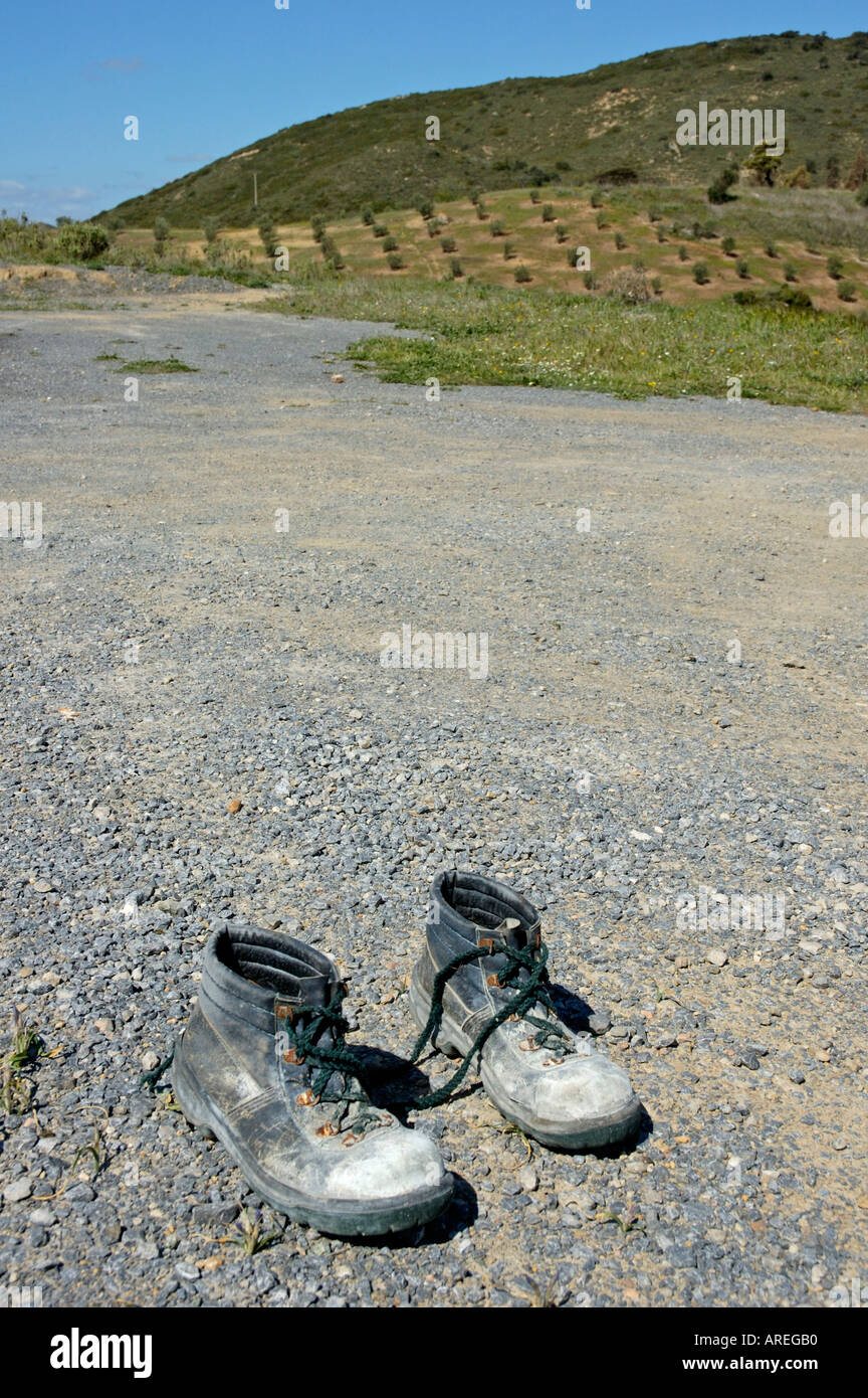 Vecchio paio di indossare gli stivali fuori seduta su terreni sassosi di asfalto. Foto Stock