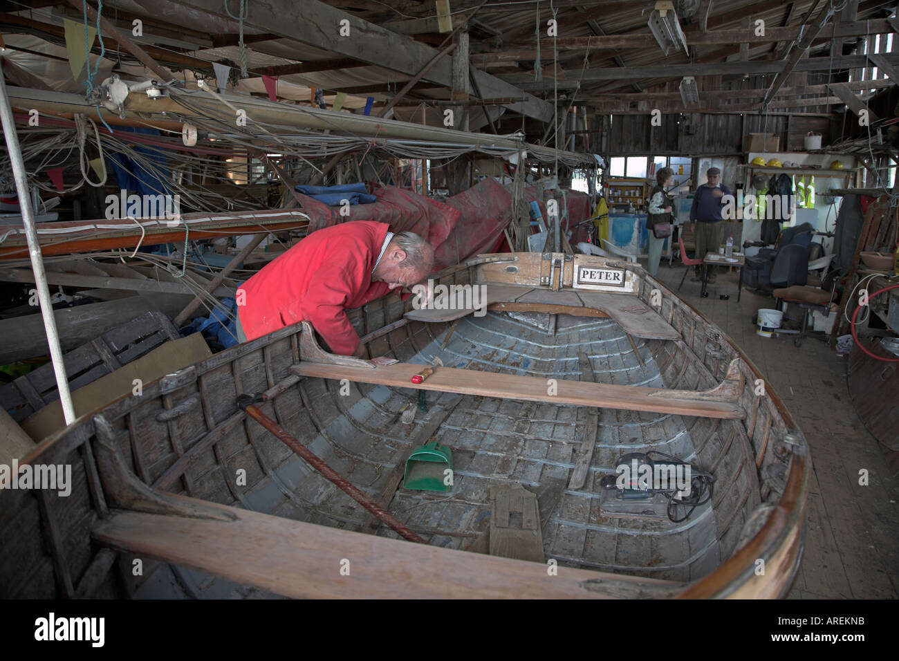 Uomo che ripara una piccola barca di legno in cantiere tradizionali, Woodbridge, Suffolk, Inghilterra Foto Stock