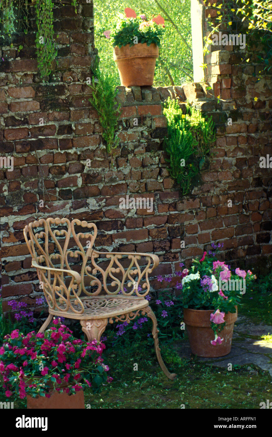 Antico muro di mattoni di lacy sedia di ferro e vasi con fiori che sbocciano nella storica Afton Villa Giardini, Louisana. Foto Stock