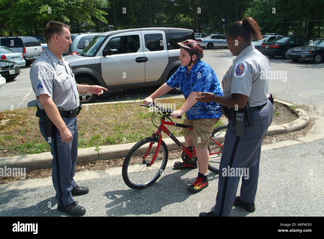 Maschio e femmina degli ufficiali di polizia di parlare a un bambino su una bicicletta per circa la sicurezza di bicicletta in Bowie Md USA Foto Stock