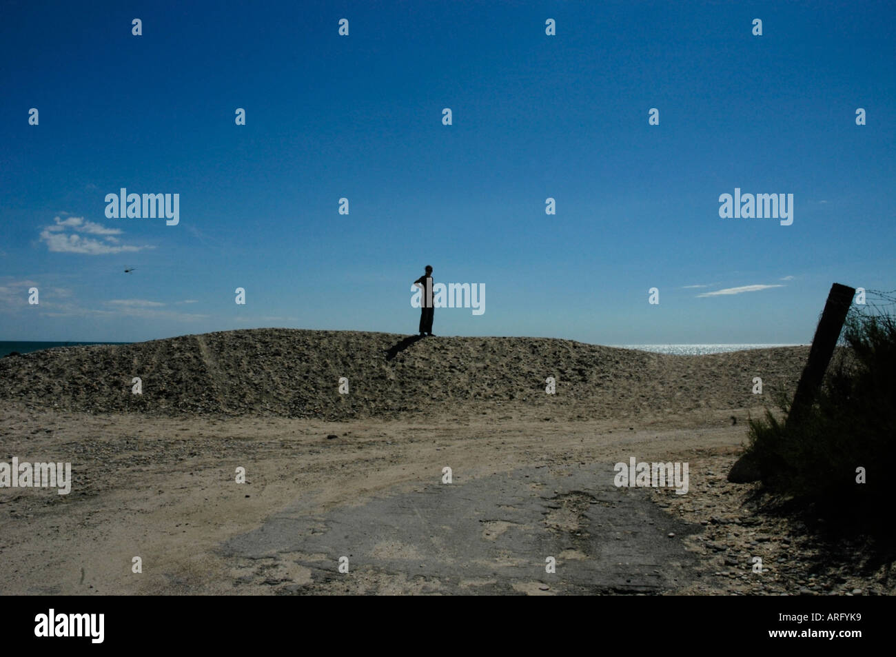 Una solitaria figura femminile si erge,stagliano contro un cielo blu chiaro sulla cima di una duna di sabbia Foto Stock