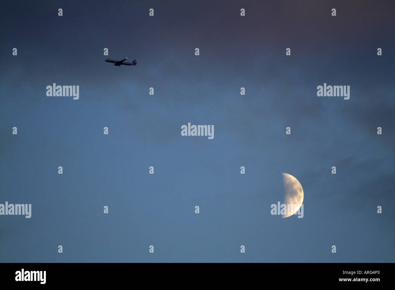 In un cielo crepuscolo di un aereo di linea vola alto al di sopra di un luminoso quarto di luna Foto Stock