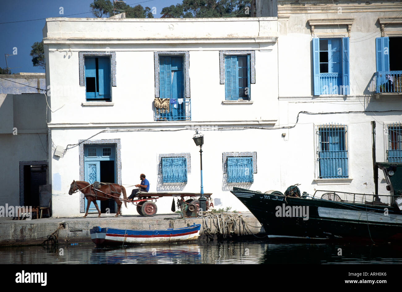 Un locale uomo alla guida di un cavallo disegnato carrello oltre la facciata con copertura di uno del blu e del bianco delle case di medina sfrangiare il vecchio porto corsair di Bizerte Foto Stock