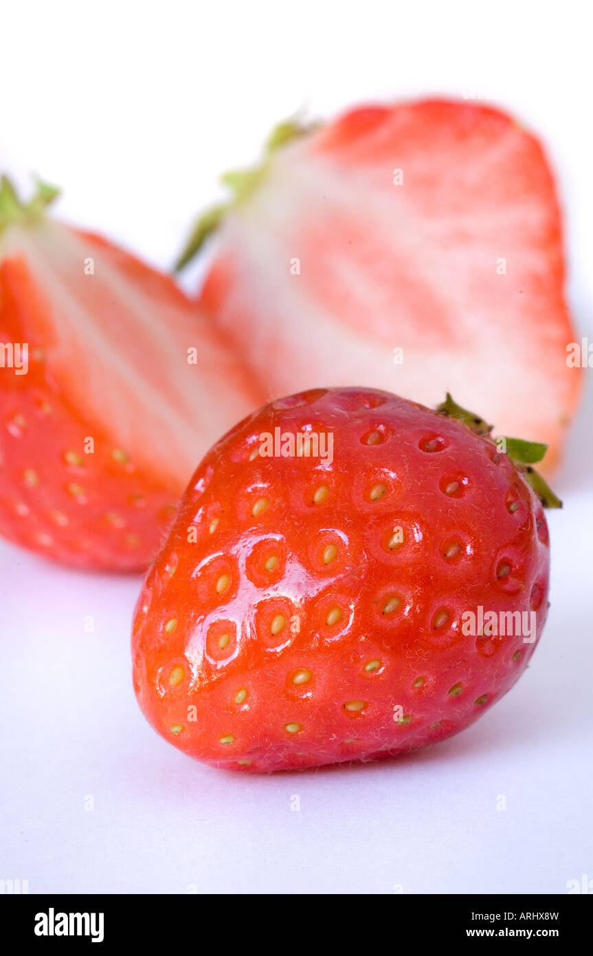 Un lucido rosso fragola organico contro il bianco con una frutta tagliata defocalizzata in background Foto Stock