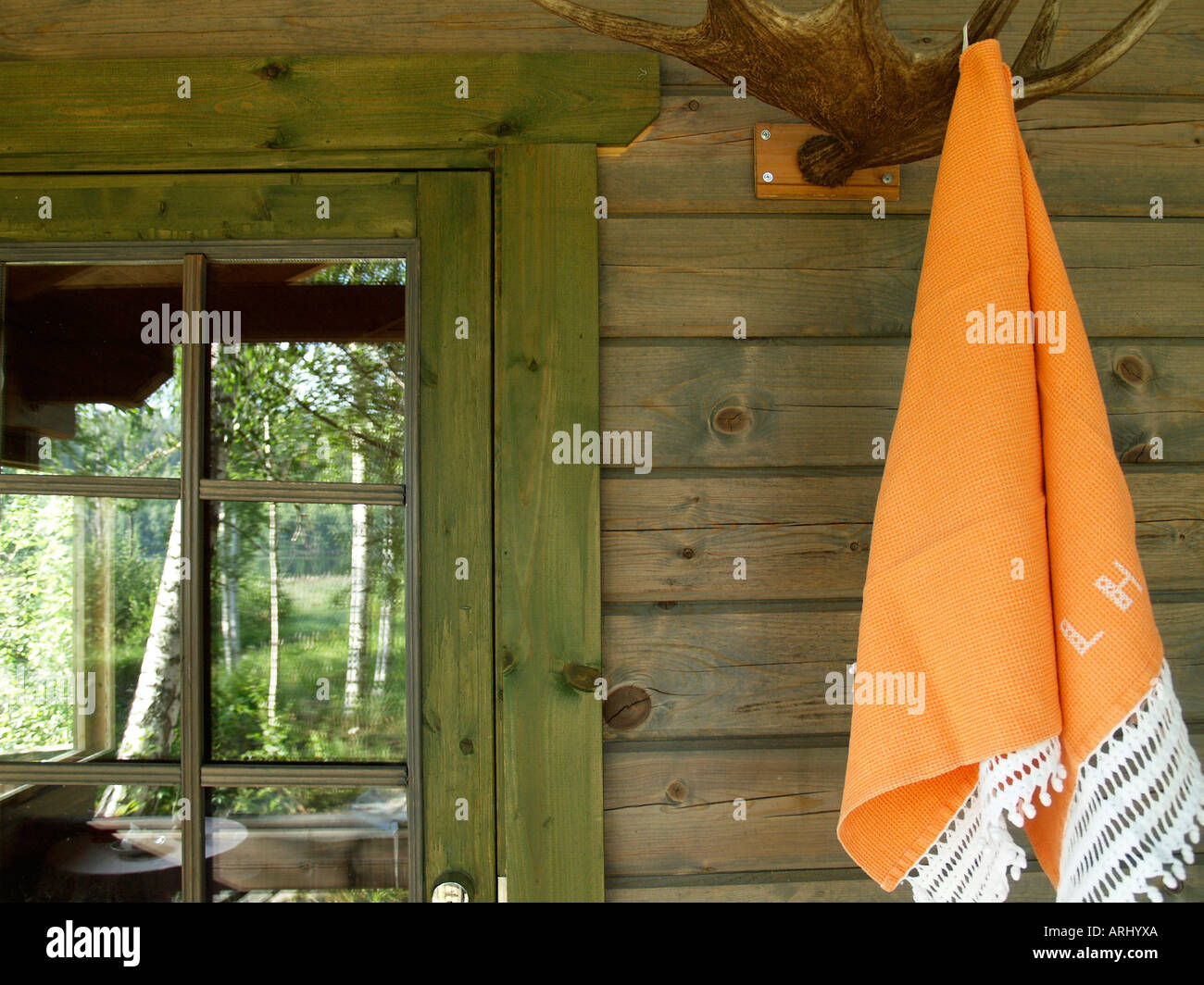 Orange asciugamani per sauna appesa al gancio costituito da corna di alce sulla parete di una sauna cottage betulle un lago a riflettere su un vento Foto Stock