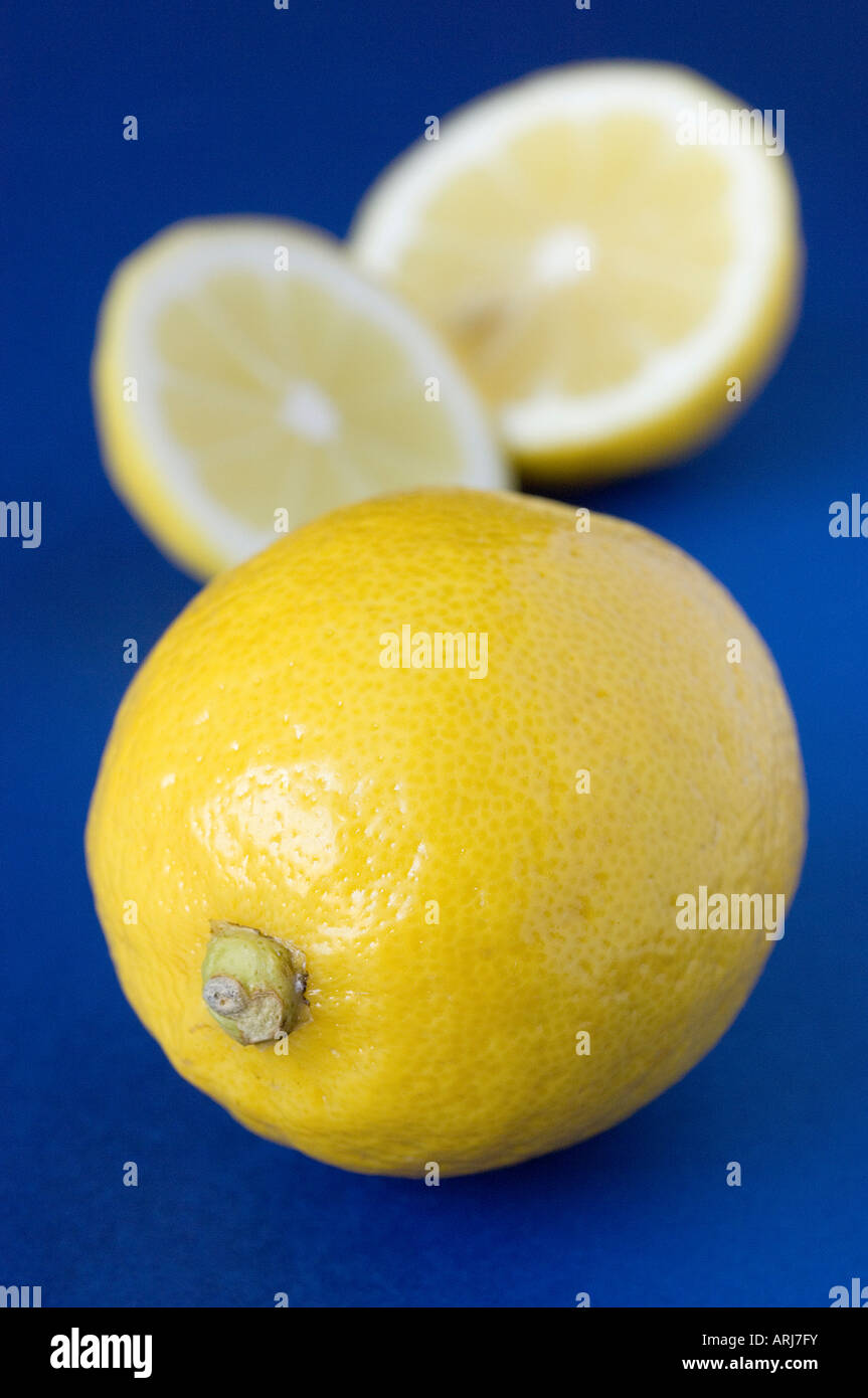 Un intero fresco limone organico con un defocalizzata, frutta tagliata in background contro blu Foto Stock