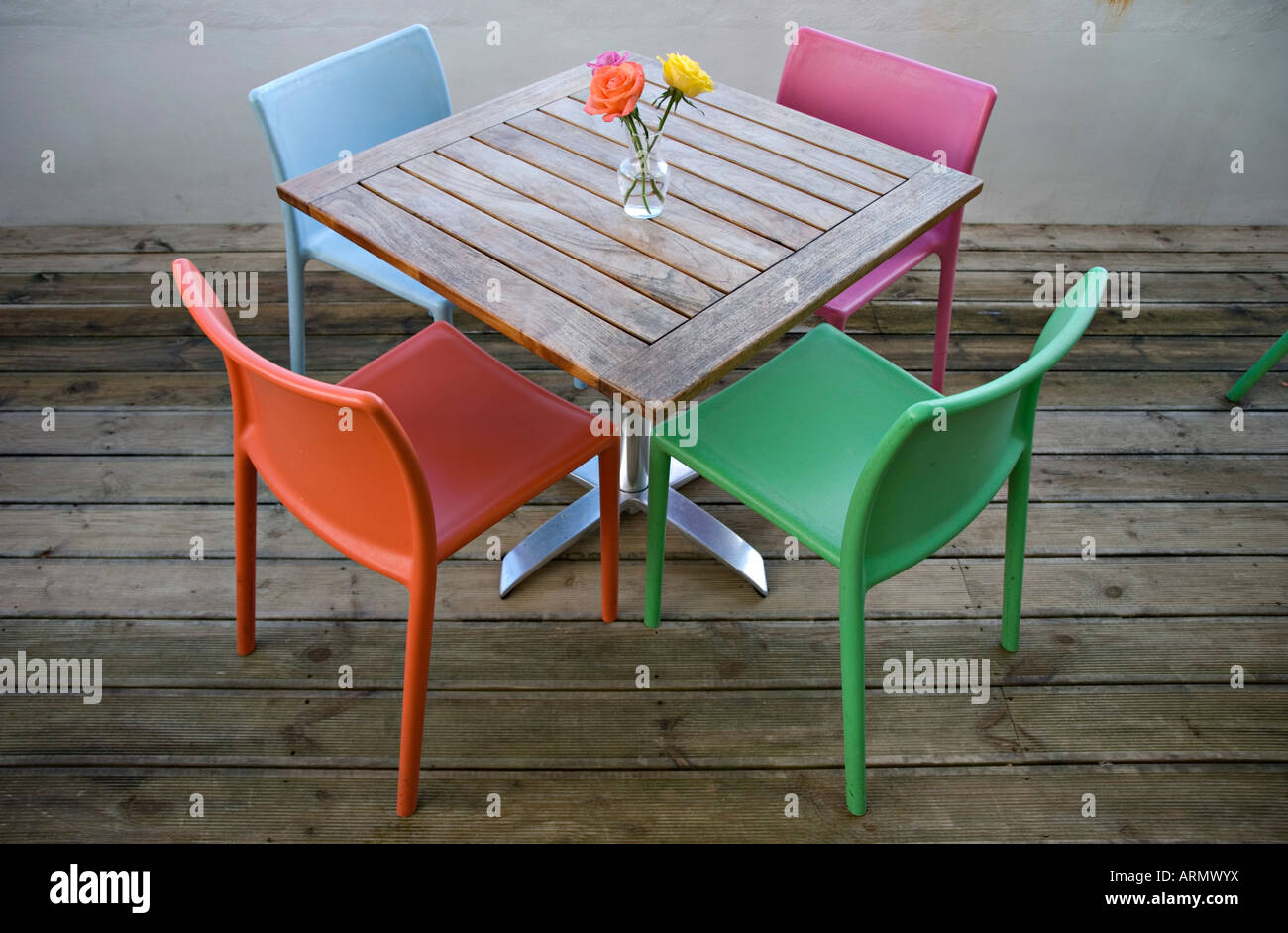 Colchester, Regno Unito. Un caffè in legno tavolo con rose e quattro sedie colorate Foto Stock