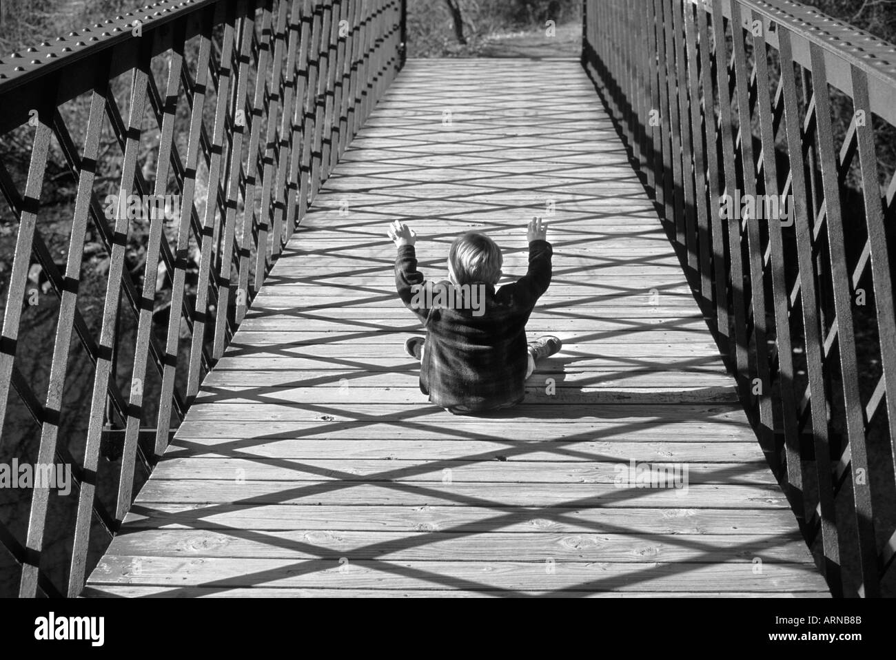 Piccolo Ragazzo seduto sul ponte con le braccia in alto Foto Stock
