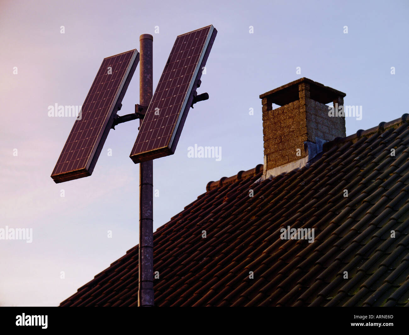 Due piccoli pannelli solari montati su un palo con un tetto in background alternativi di alimentazione di energia Foto Stock