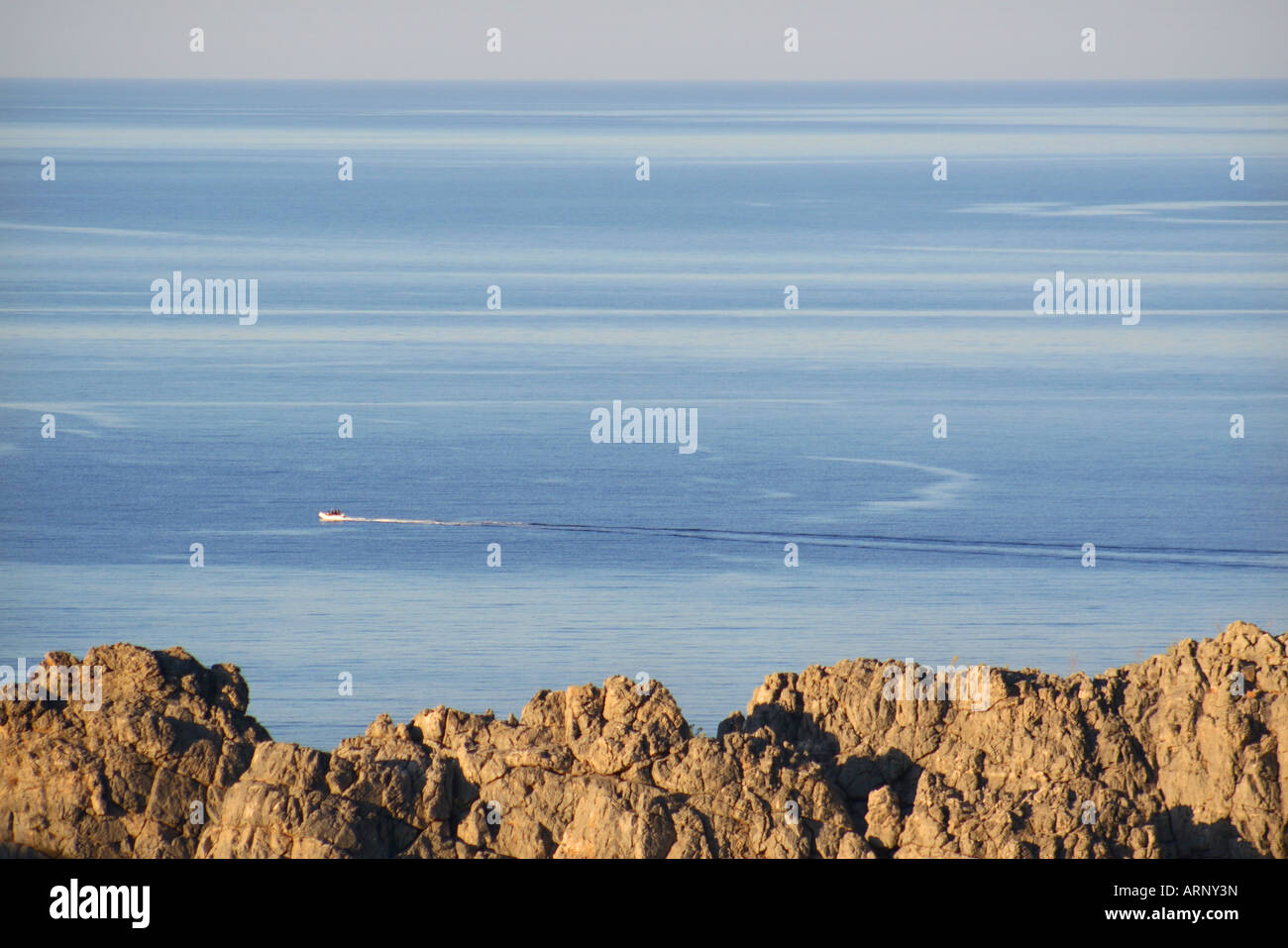 Barca motori attraverso il blu mare Mediterraneo con il roccioso paesaggio greco in primo piano Rodi Grecia Foto Stock