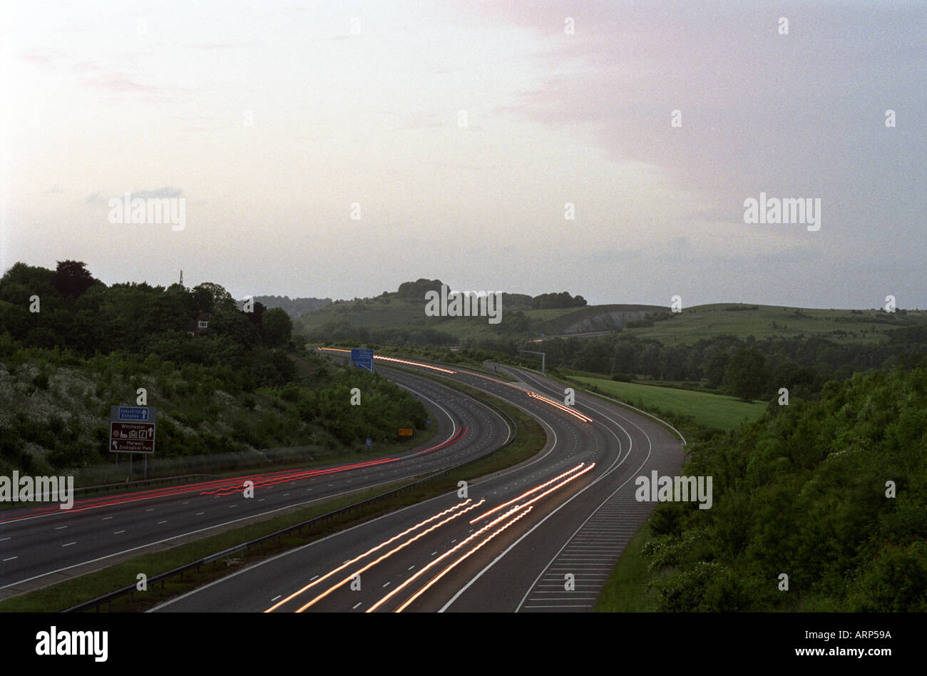 Striature di movimento hanno offuscato le luci dell'automobile sull'autostrada M3 mentre si avvicina a Twyford tagliando dal sud al crepuscolo. Twyford Cutting, Hampshire, Regno Unito. Foto Stock