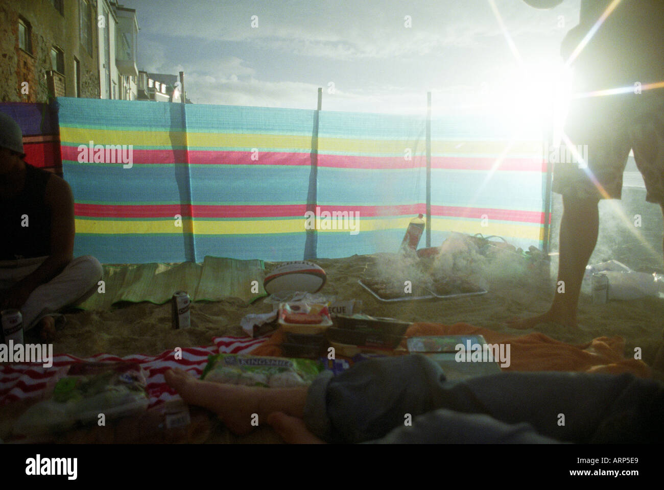 Spiaggia con asciugamani, barbecue, cibo, stuoie da spiaggia in paglia e finestra retroilluminata e dai colori vivaci. St. Ives, Cornovaglia, Regno Unito. Foto Stock