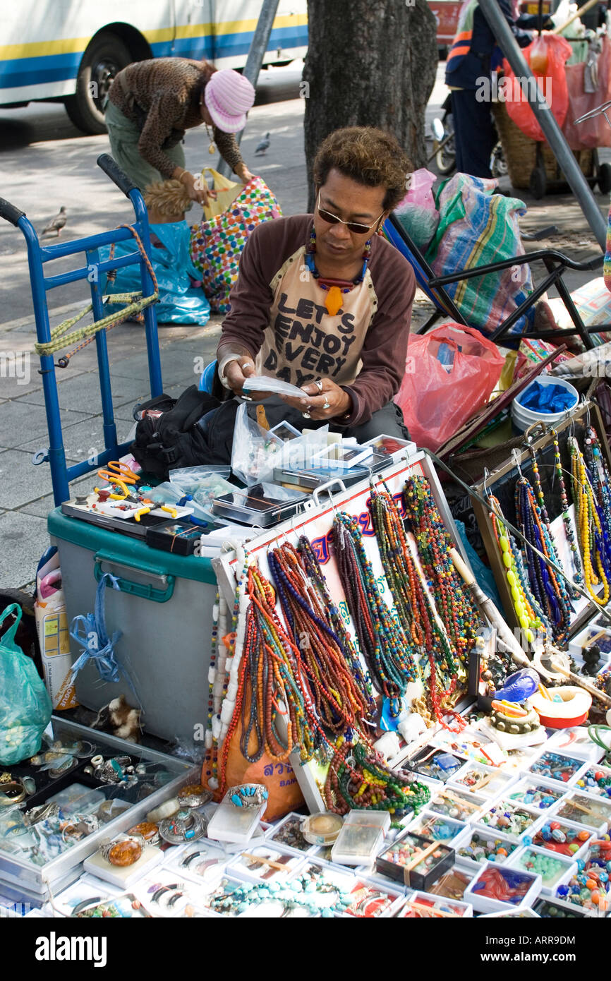 Un venditore ambulante su una strada a Bangkok disponendo i suoi beni per la visualizzazione Foto Stock