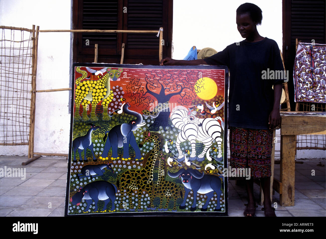 Un bottegaio che mostra un acrilico dipinto da un artista locale in Stone Town Zanzibar Tanzania Africa orientale Foto Stock
