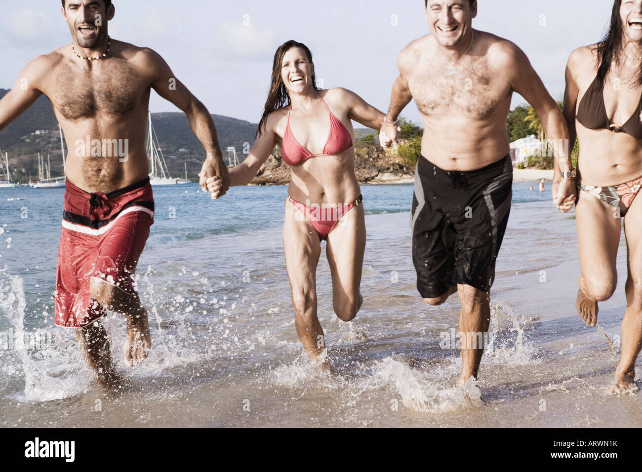 Due metà coppie di adulti tenendo le mani e correre sulla spiaggia Foto Stock