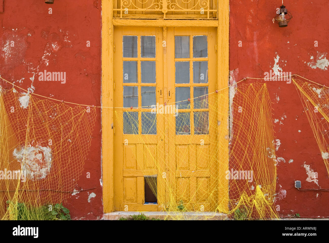 Vecchio edificio con pannelli di vetro giallo porta di legno fornisce il contesto ideale per appendere il giallo delle reti da pesca ad asciugare, Kamini, Hydra Island, Grecia Foto Stock