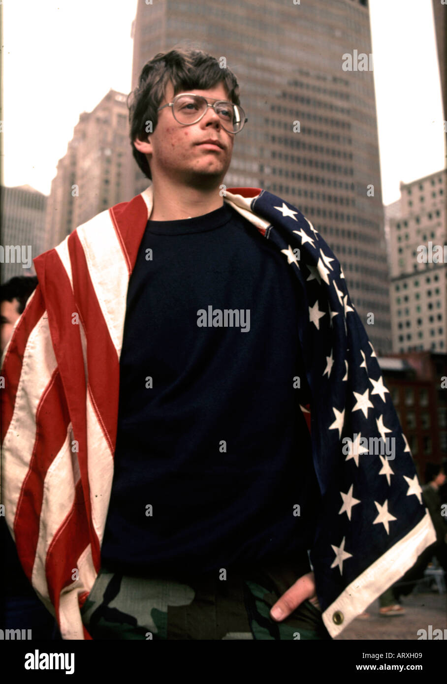 Patriotic giovane con una bandiera americana drappeggiati oltre le sue spalle lungo il Memorial Day Parade rotta in New York City NY Foto Stock