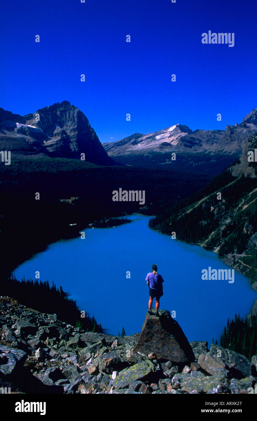 Escursionista in piedi su una roccia che si affaccia su un cristallo blu del lago e delle montagne sullo sfondo Foto Stock Escursionista in piedi su una roccia che si affaccia su un cristallo blu del lago e delle montagne sullo sfondo Foto Stock