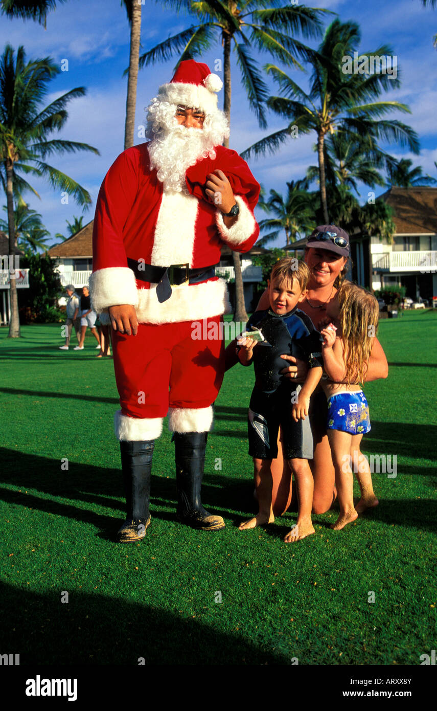 Su un grande prato erboso sul lato sud di Kauai, un uomo vestito da Santa Claus si erge nei pressi di una donna e due bambini piccoli Foto Stock