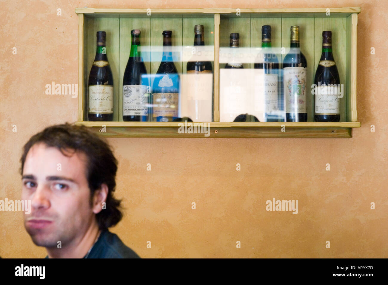 Colpo alla testa di un maschio caucasico e un montato a parete armadio in legno contenenti bottiglie di vino Foto Stock