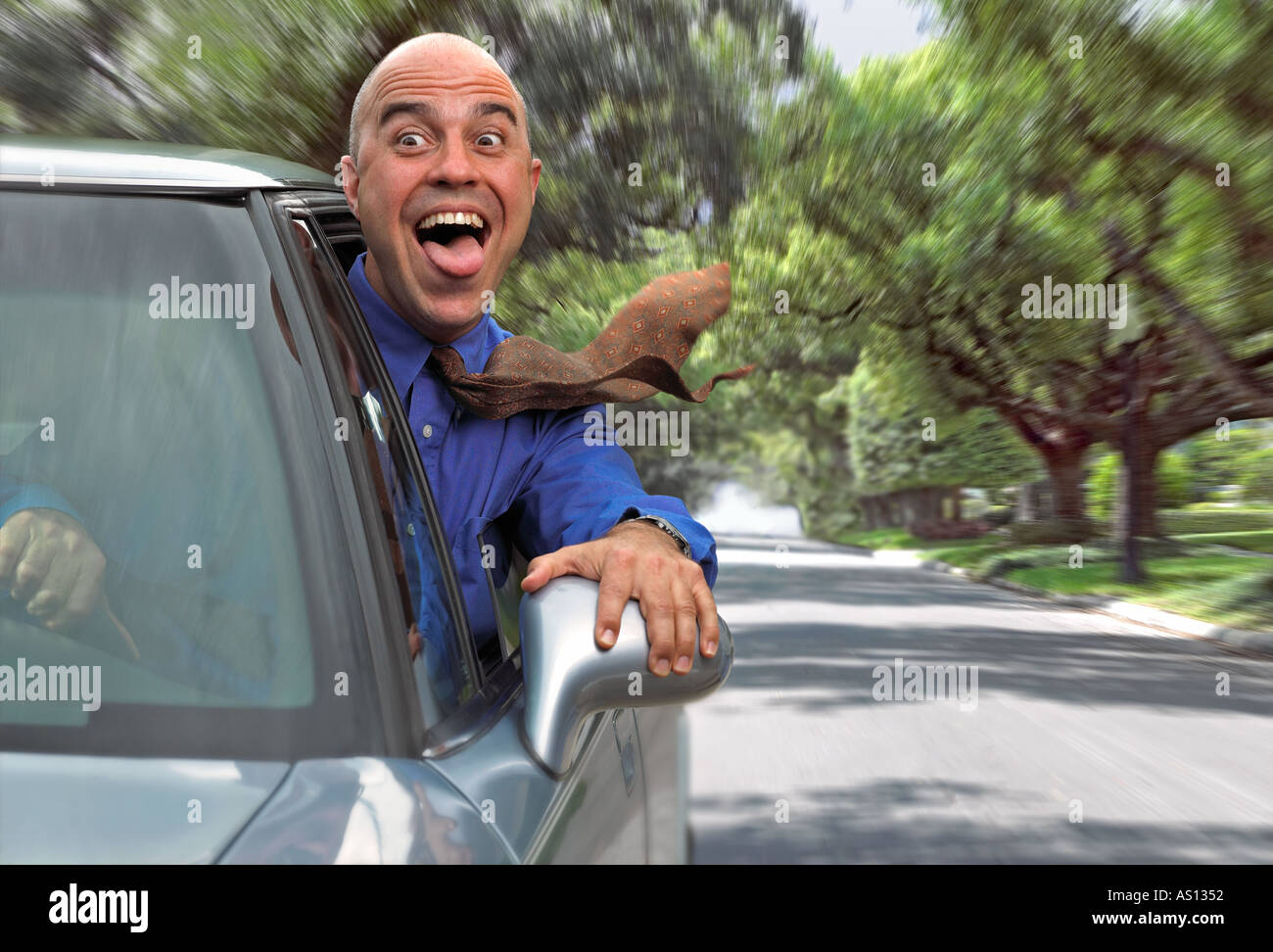 Crazy uomo felice con la bocca aperta e la lingua di fuori si affaccia alla finestra mentre si guida la sua auto giù per una strada alberata Foto Stock