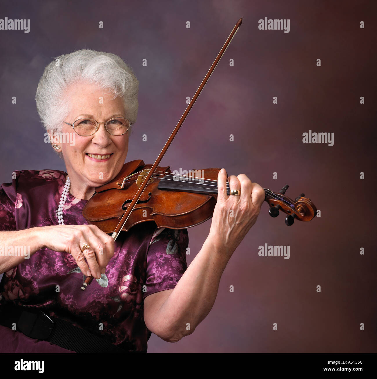 Senior donna caucasica suona il violino mentre sorridente contro modellato sullo sfondo Foto Stock