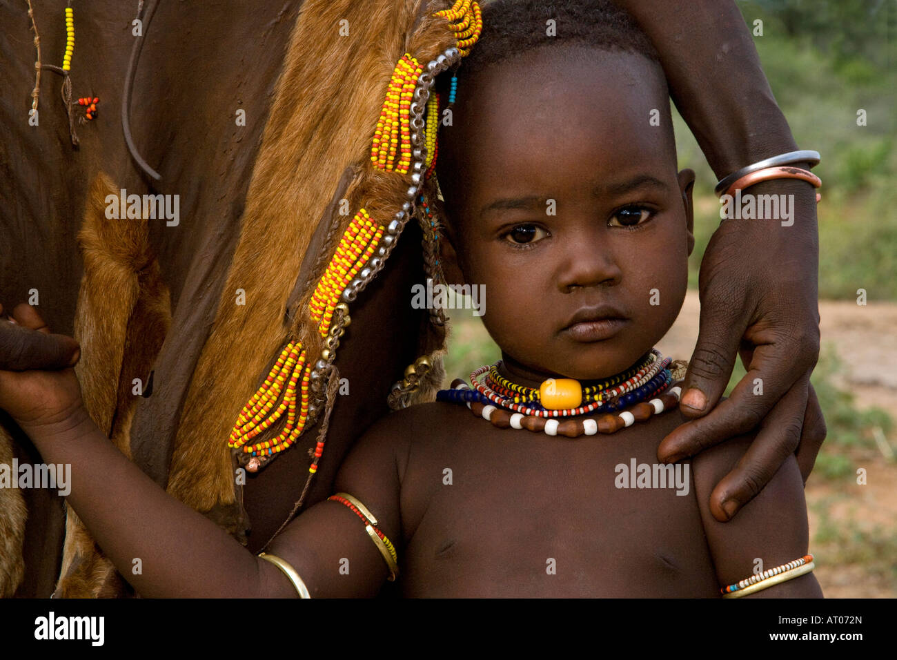 Bella timida ragazzina della tribù Hamer detiene sulla sua madre, Omo River Valley, Etiopia Foto Stock