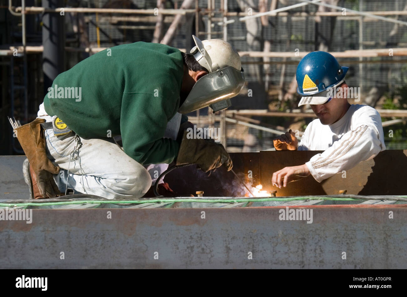 Due uomini in un duro cappelli, lavora in un cantiere. Uno dei lavoratori indossa una maschera facciale protettiva durante la saldatura a punti. Foto Stock
