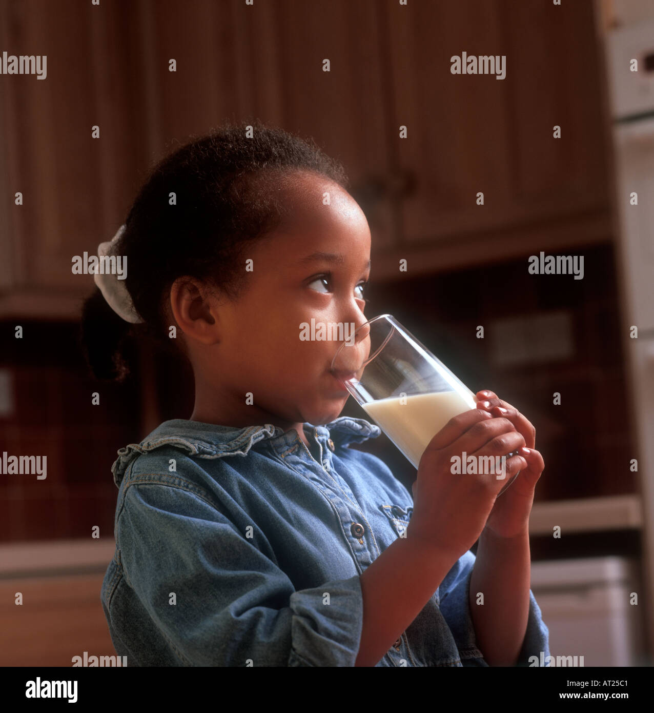 Afro-caraibica ragazza infantile 3-5anni bere un bicchiere di latte nella sua cucina domestica Foto Stock