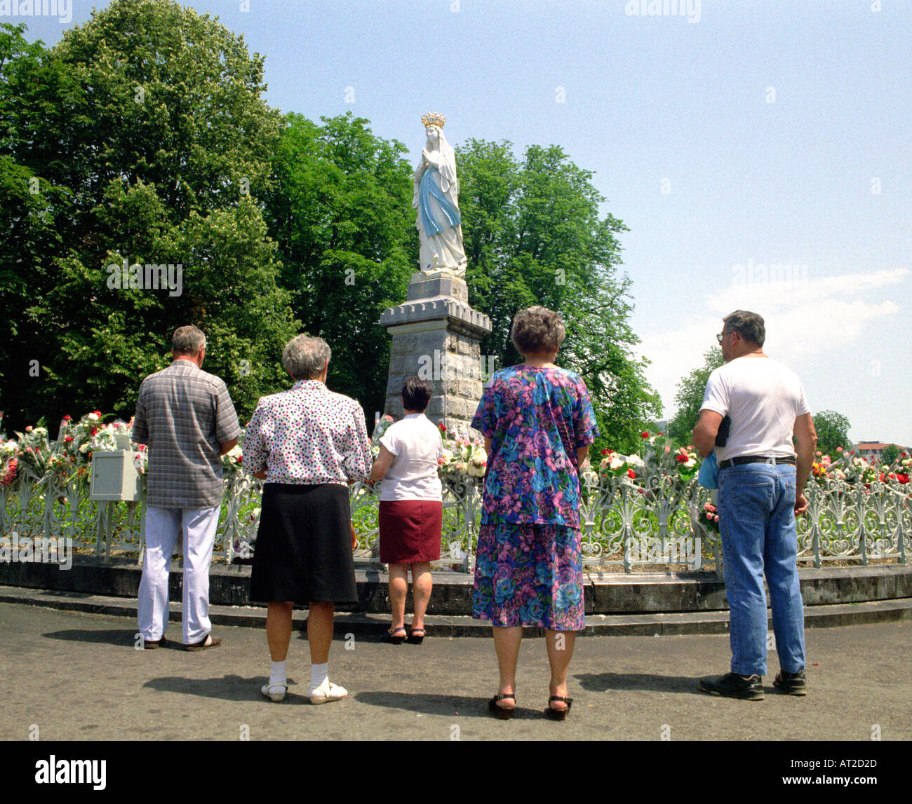 I turisti si sono riuniti attorno a una statua nei giardini dei Santuari di Notre Dame de Lourdes nel sud-ovest della Francia Foto Stock