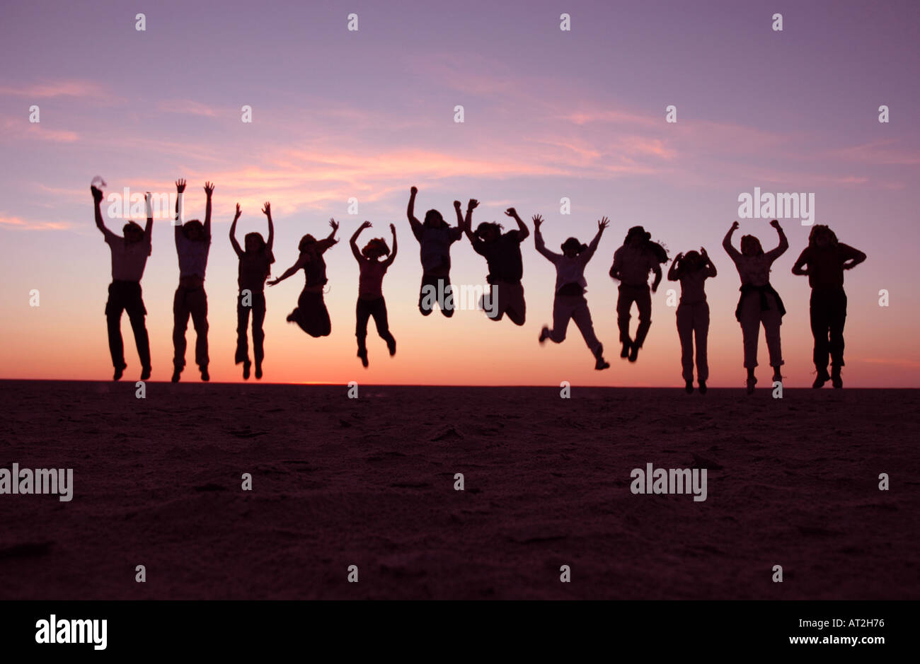 Gruppo di persone che saltano al tramonto sulla coppa di sale nel Kalahari Botswana Sud Africa Foto Stock