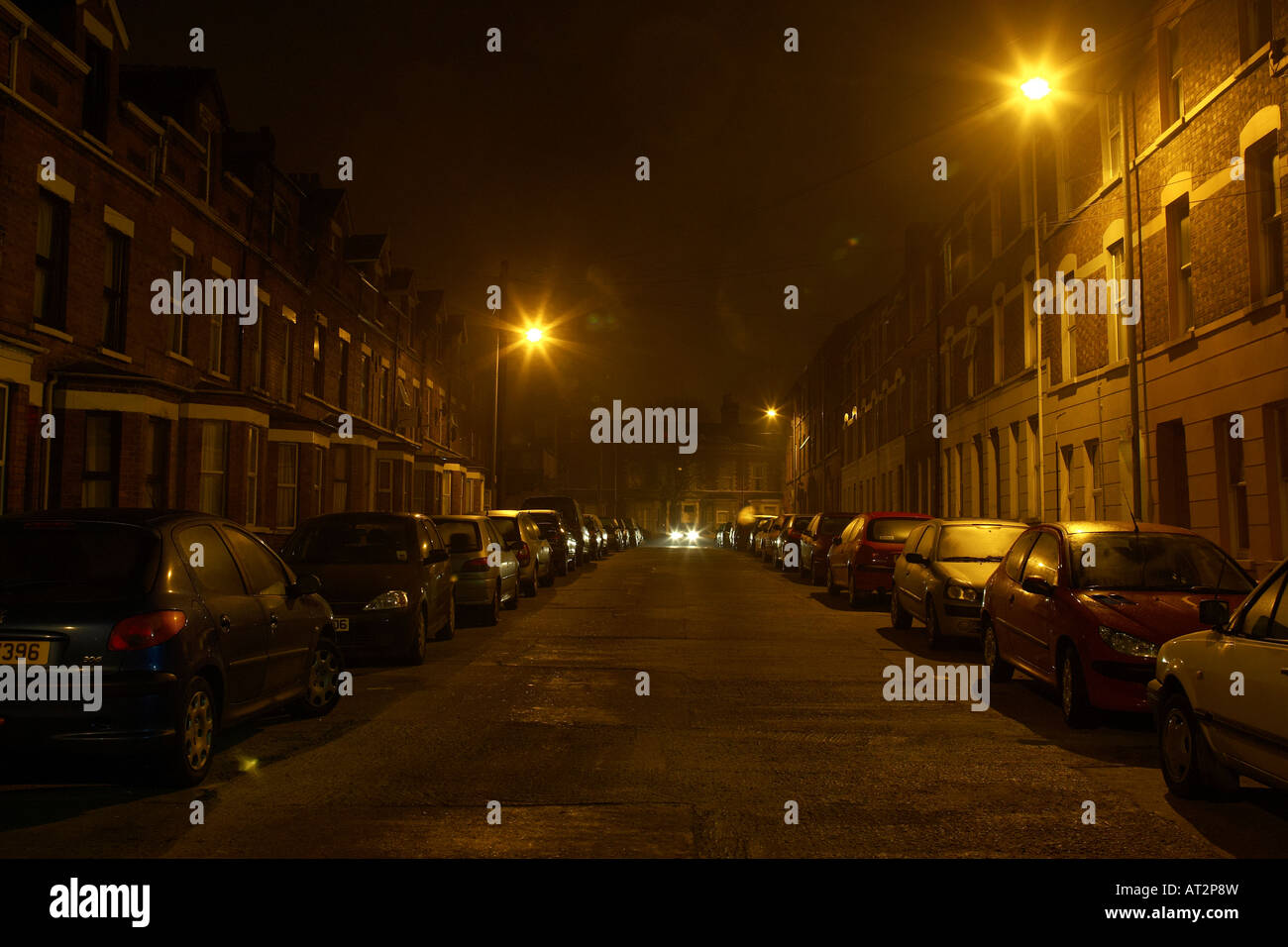 Auto si avvicinano al centro di una stretta e buia strada notturna a Belfast Foto Stock