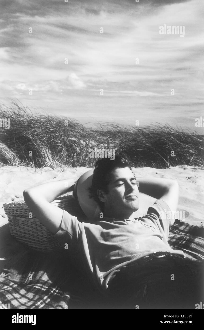 Un uomo disteso al sole, in appoggio su un cesto da picnic Foto Stock