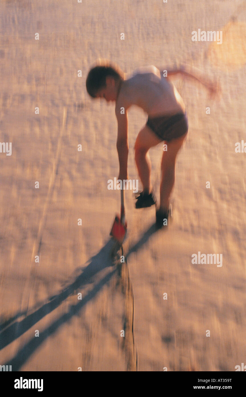 Un ragazzo che segna nella sabbia con una vanga Foto Stock