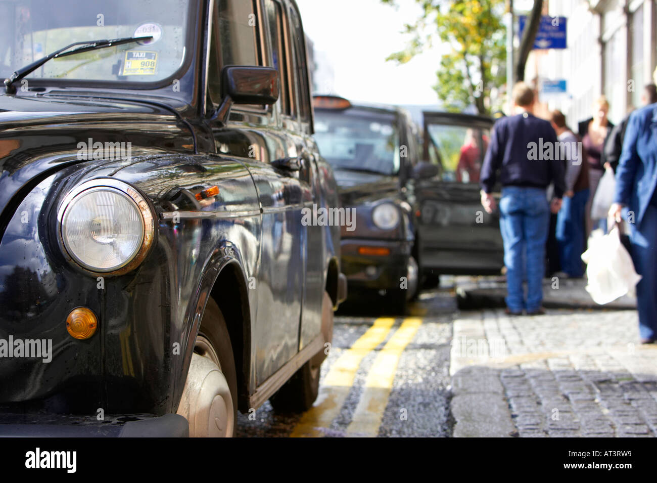 Fila di nero hackey Londra trasporto taxi su un rango in Belfast City Centre con il tassista tenendo lo sportello aperto per il trasporto di passeggeri Foto Stock