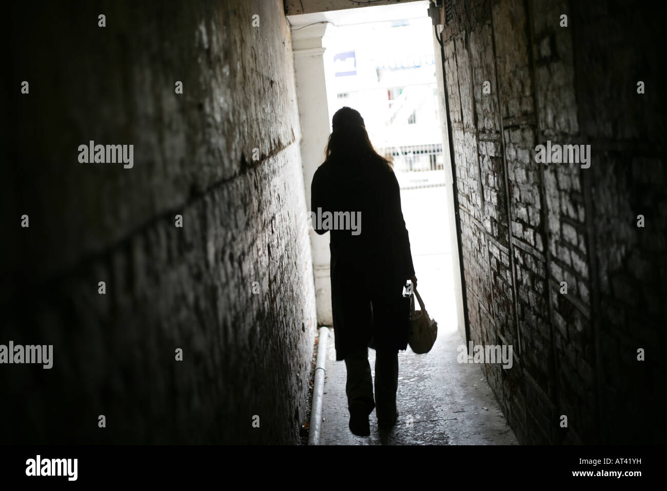 Un irriconoscibile donna cammina da solo verso il basso un vicolo buio portando la borsetta Foto Stock