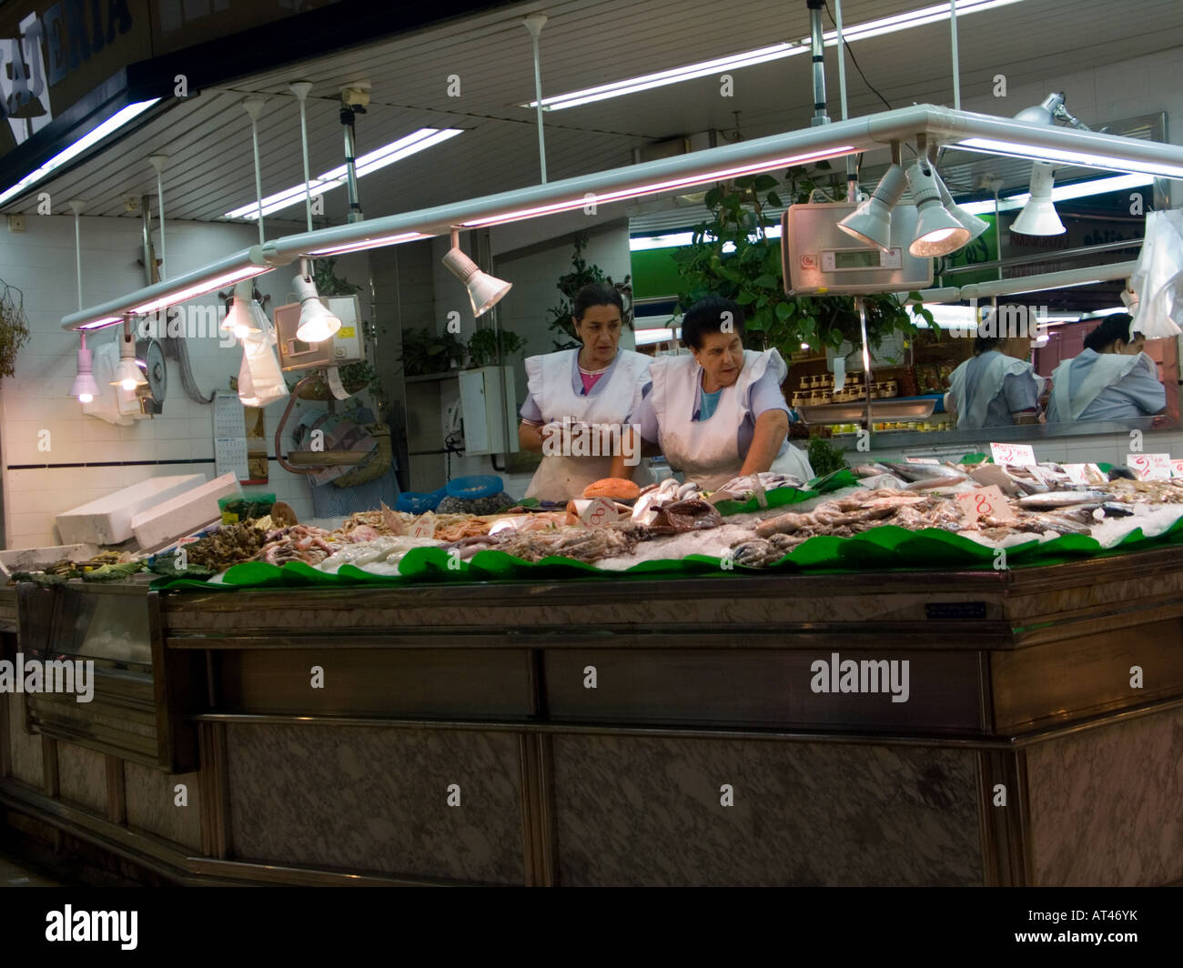 Due lady venditori di pesce indossando grembiuli frilled facendo il bilancio su una fase di stallo nel Mercato Centrale edificio, Reus, Spagna Foto Stock