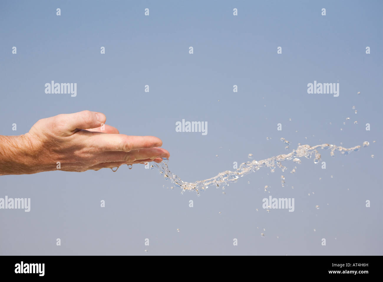 Acqua di essere gettato in aria da mani contro un cielo blu Foto Stock