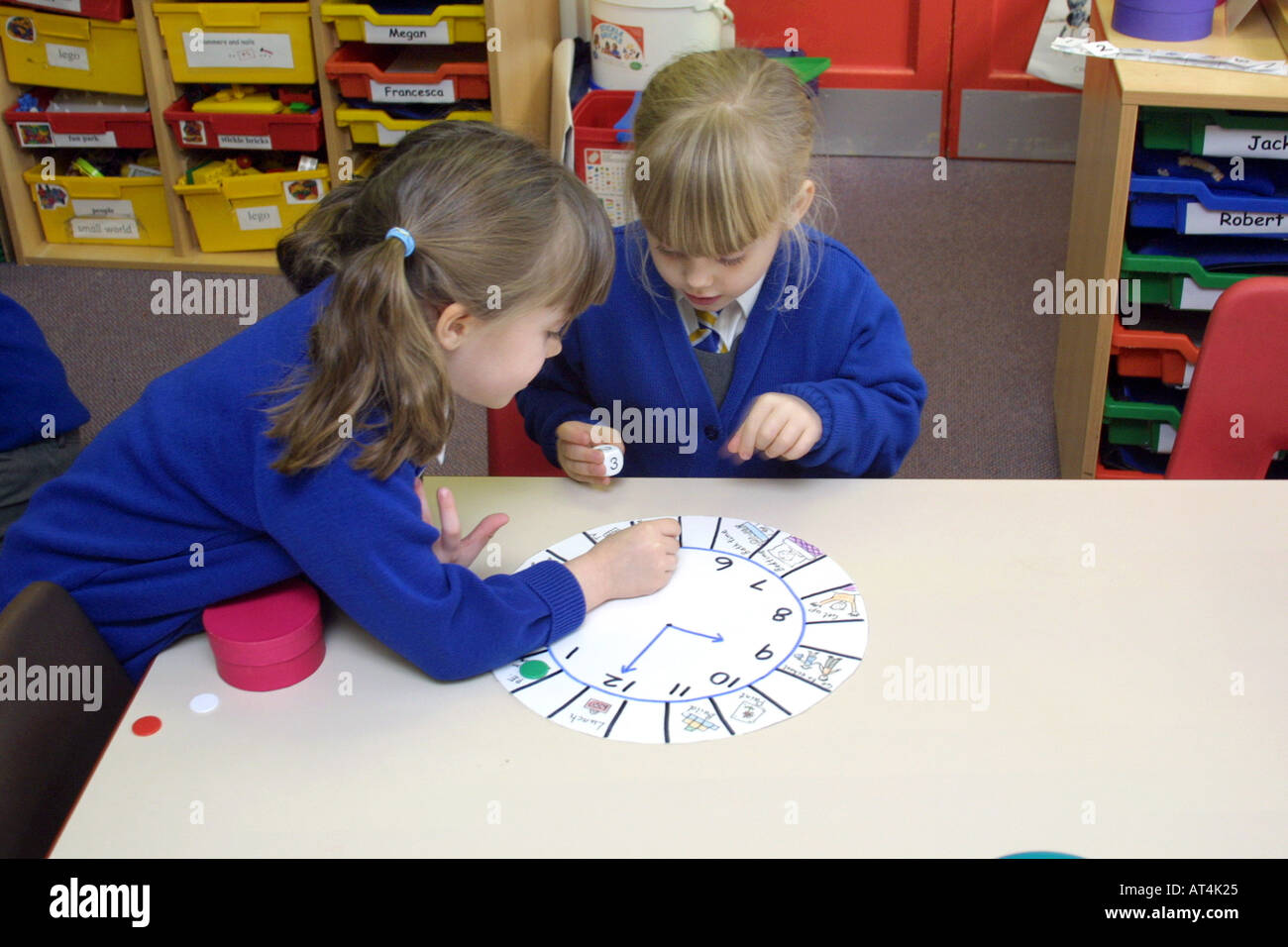 Due giovani ragazze in classe di ricezione di imparare a leggere il tempo attraverso il gioco Foto Stock