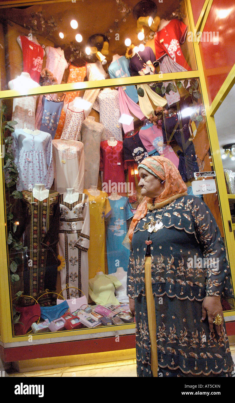 Donna con la copertura del capo passeggiate su Alessandria d Egitto street nella parte anteriore del negozio vestito con abiti sul display nella finestra Foto Stock