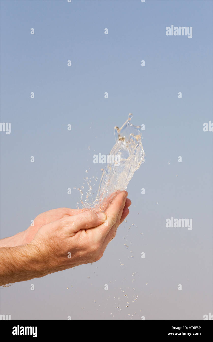 Acqua di essere gettato in aria da mani contro un cielo blu Foto Stock