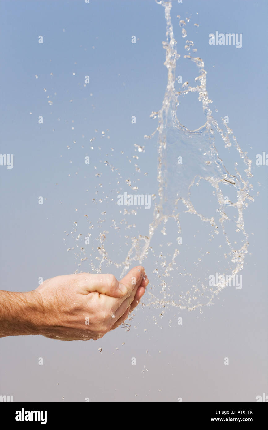 Acqua di essere gettato in aria da mani contro un cielo blu Foto Stock
