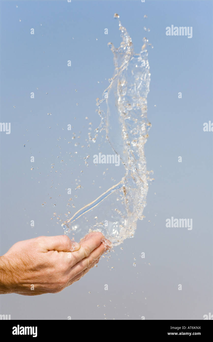 Acqua di essere gettato in aria da mani contro un cielo blu Foto Stock