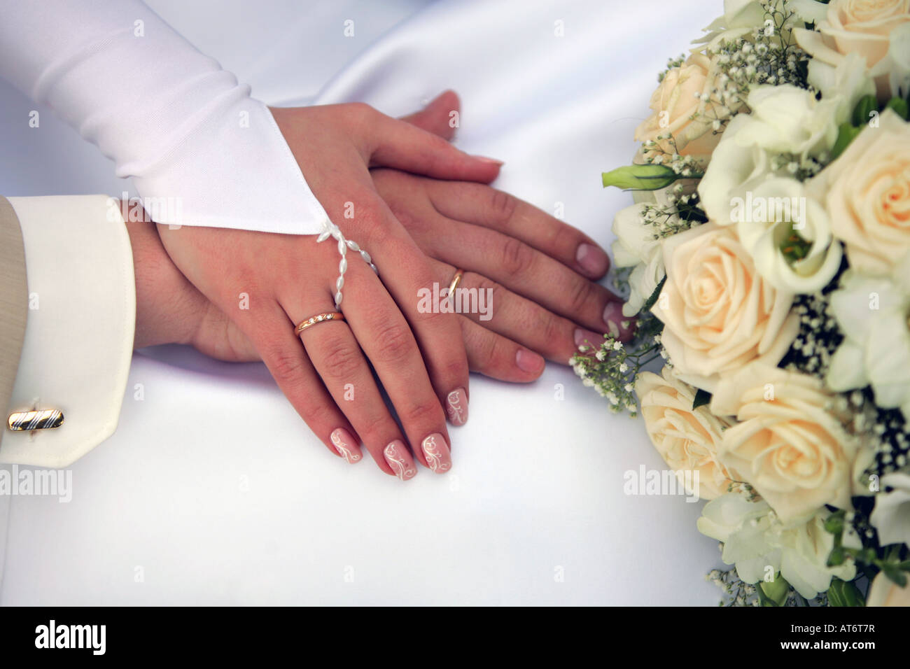 Un ritratto di una sposa giovane tenendo le mani per mostrare le loro fedi accanto a un mazzo di fiori sul womans w bianco Foto Stock