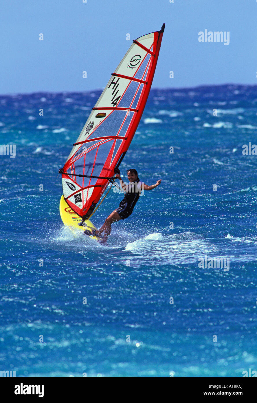 Una giovane donna windsurf prende un emozionante giro sul mare azzurro a Kahana Beach Park sull'isola di Maui. Foto Stock