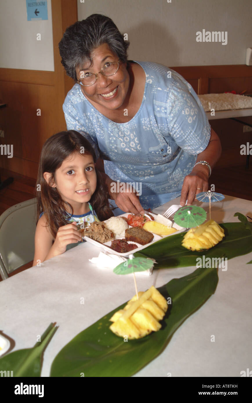 Donna locale sorrisi come ragazza giovane ottiene pronto a mangiare la sua piastra di luau a Fundraiser annuale. Accademia del Pacifico a Honolulu Foto Stock